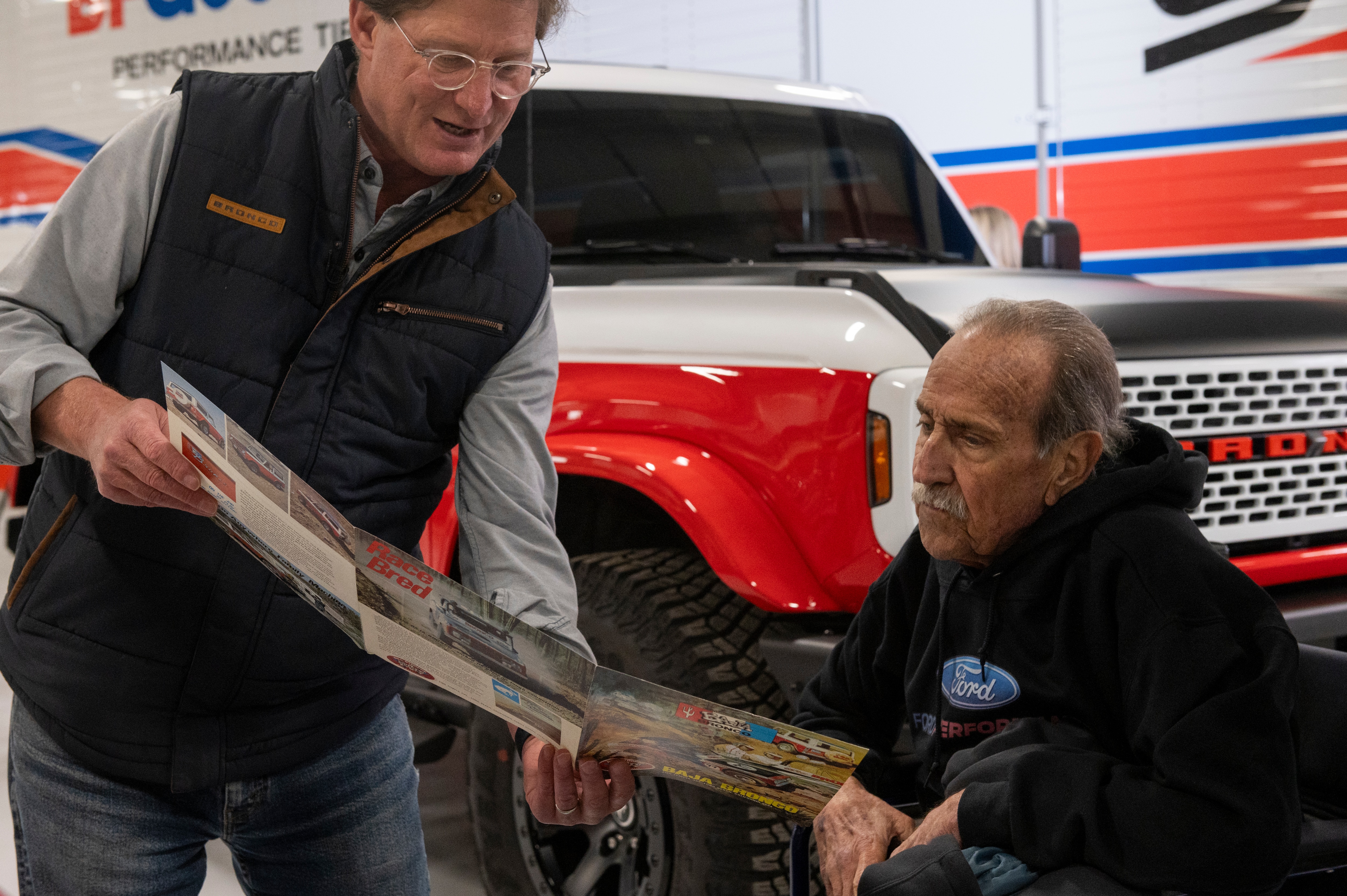 From left, Ted Ryan, archives and heritage brand manager at Ford Motor Co., shows Willie Stroppe historical items and photos while standing next to the new Ford Stroppe Bronco, on Tuesday, Feb. 6, 2024 in Johnstown, Colorado. Rachel Woolf for Ford